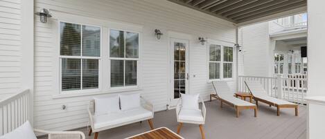 A covered porch with white railings, white furniture, and a wooden table.