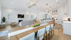 A spacious living area with a wooden dining table, light blue upholstered chairs, a grey sofa, and a fireplace. - Beachtown - STEPS FROM BEACH & POOL - 5 Bed, 4.5 Bath (Galveston)