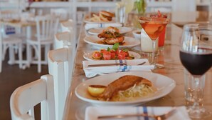 A restaurant interior with a long dining table, white chairs, and a wine rack in the background. - Beachtown - STEPS FROM BEACH & POOL - 5 Bed, 4.5 Bath (Galveston)