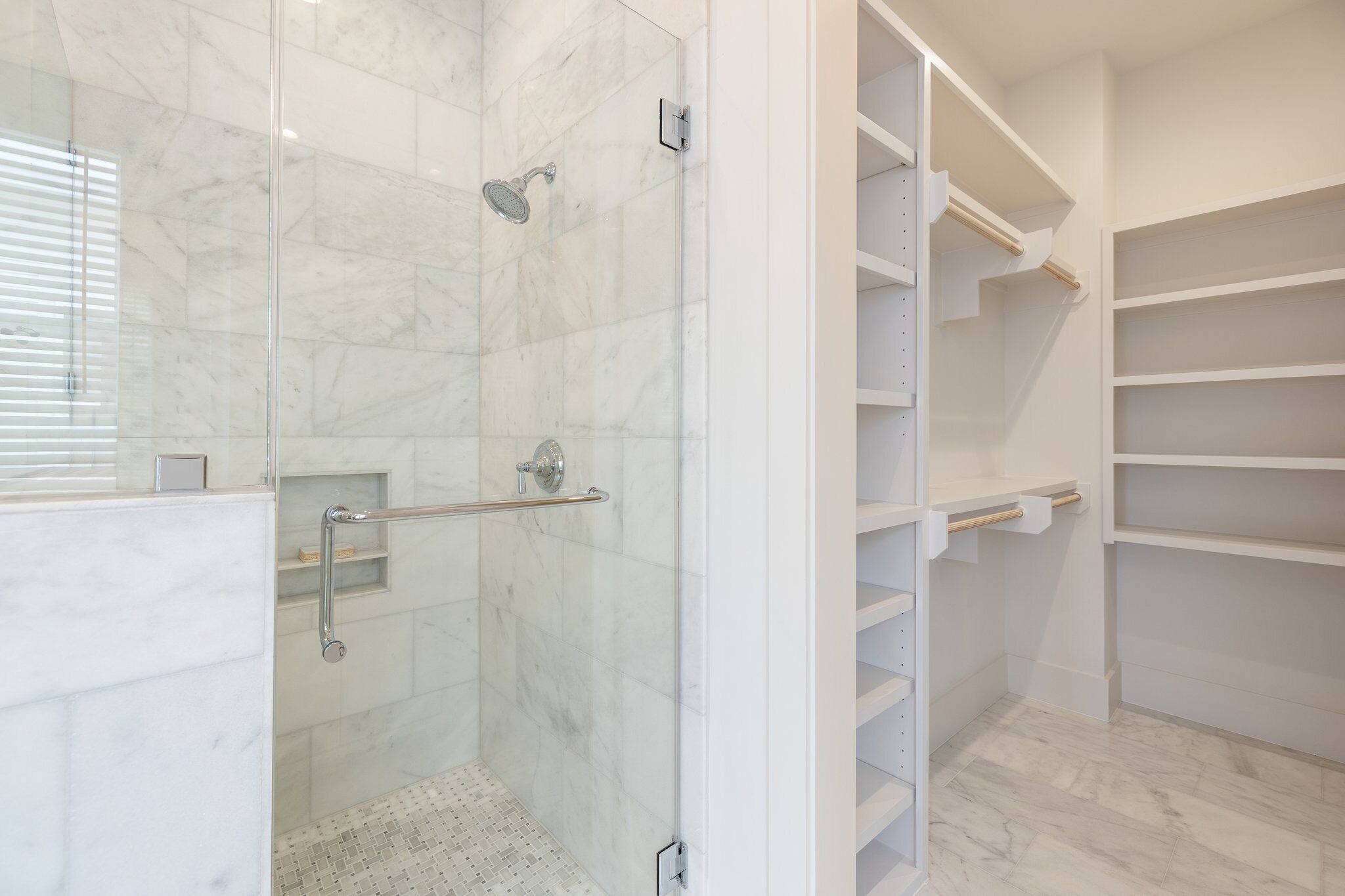 Une salle de bain moderne dotée d’une douche à parois de verre, d’un revêtement de sol en marbre et d’étagères blanches intégrées.
