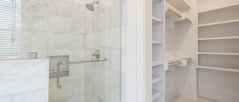 Une salle de bain moderne dotée d’une douche à parois de verre, d’un revêtement de sol en marbre et d’étagères blanches intégrées.