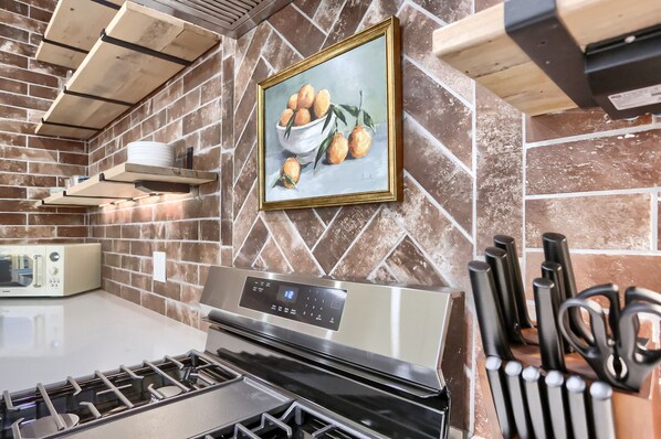 A kitchen with a modern stove, a microwave, and a brick backsplash.