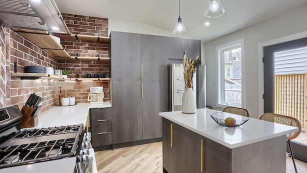Una cucina moderna con isola centrale, mobili scuri e una parete decorata con mattoni.