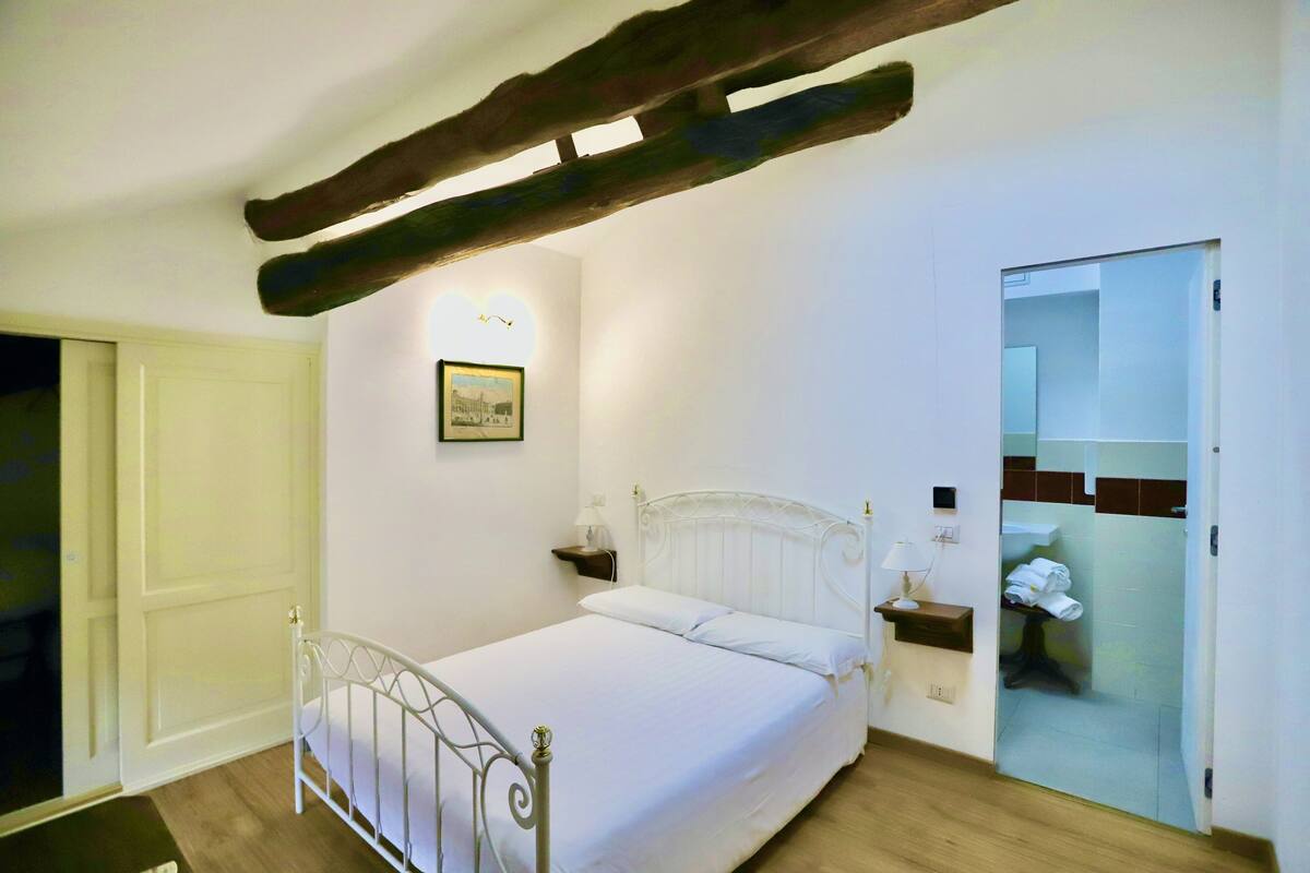 A neatly arranged bedroom with a bed, bedside tables, a framed picture, and a bathroom door.