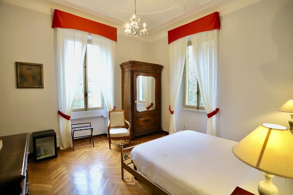 A hotel room with a bed, a chair, a wooden wardrobe, a desk, and a lamp.