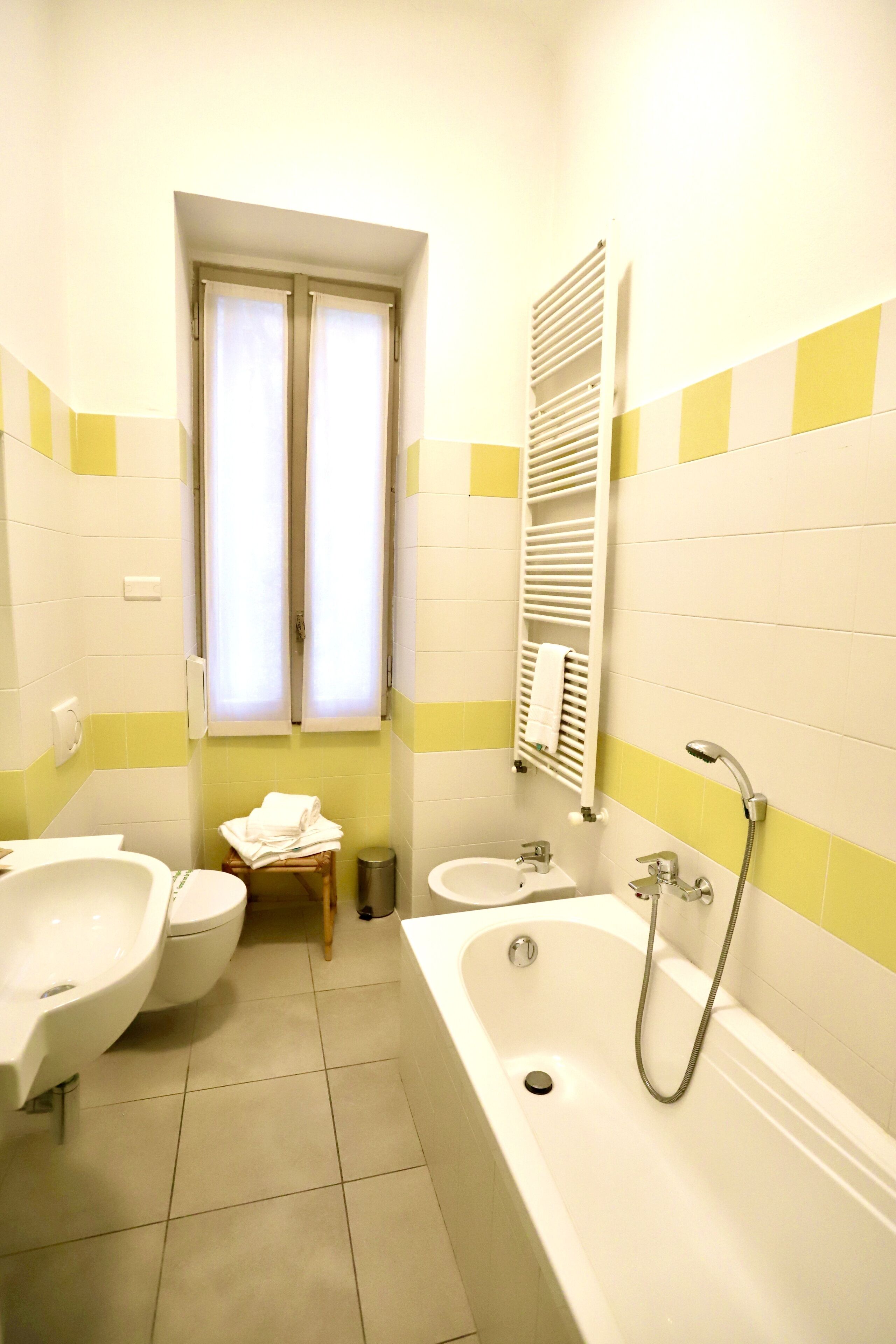 Un baño con bañera, dos lavamanos, una ventana con cortinas y un perchero para toallas.