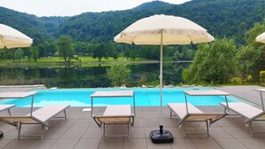 A poolside area with lounge chairs and umbrellas, a clear view of a lake and mountains in the background. - La Villa Del Lago (Valganna)