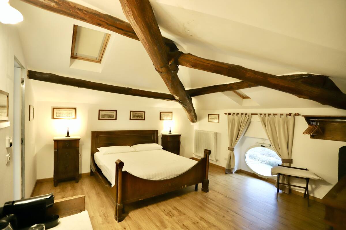 A bedroom with a wooden bed, a nightstand, a dresser, a window with curtains, and a skylight.