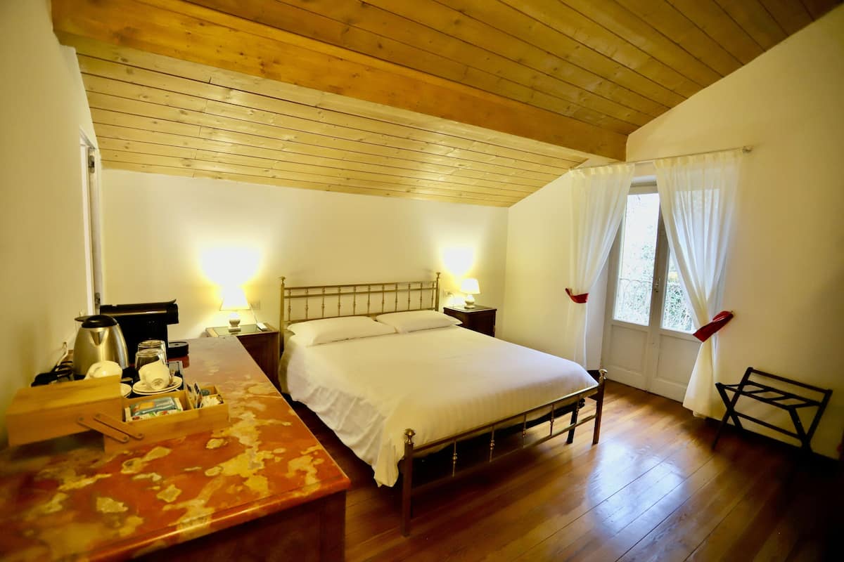 A bedroom with a wooden bed, bedside tables, a desk, and a window with curtains.