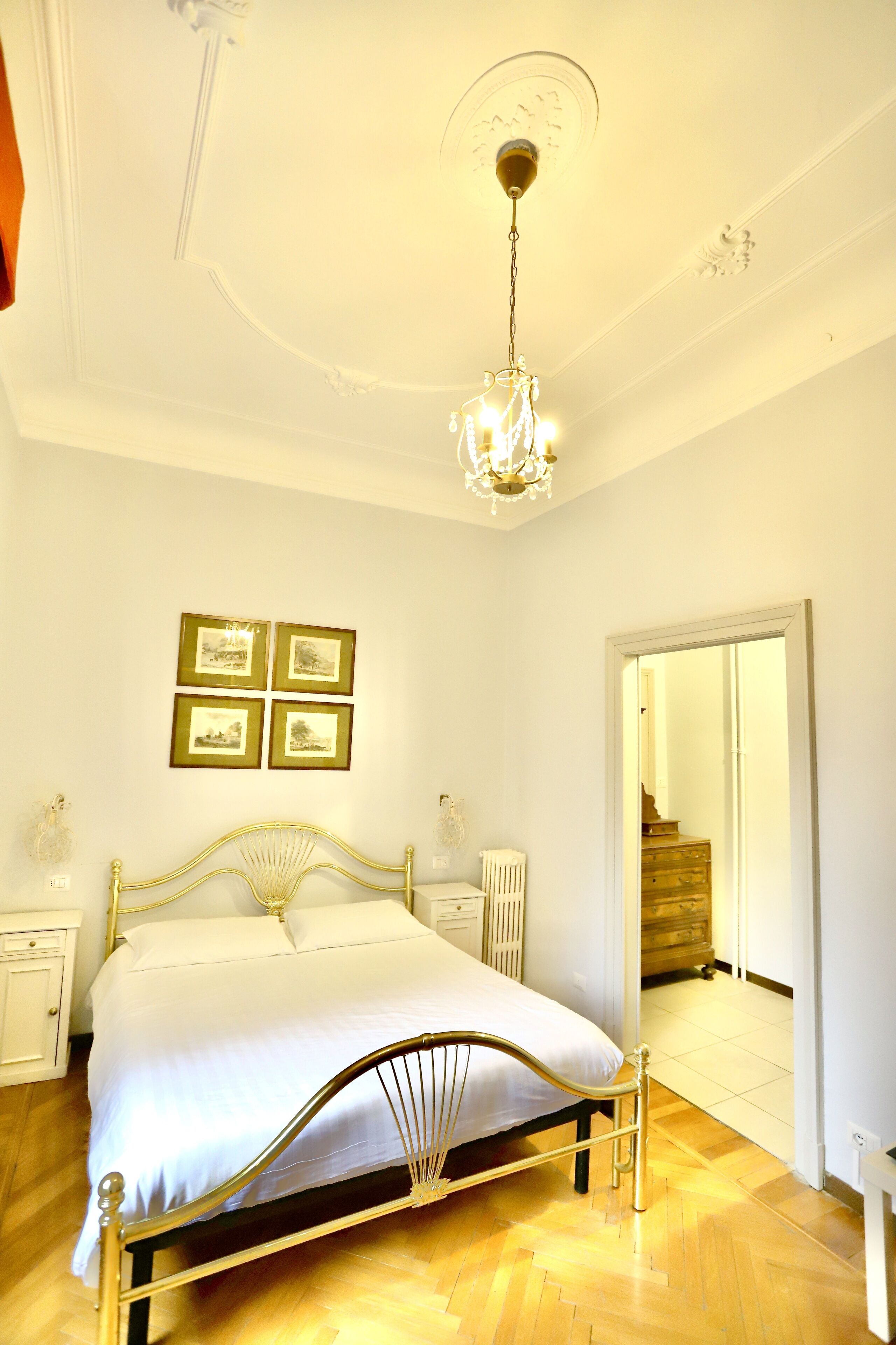 Un dormitorio con una cama, una araña, cuadros en la pared y una puerta que da a otra habitación.
