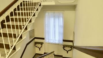 Een trap met witte leuningen en een houten handrail, leidend naar een plateau met een raam met witte gordijnen.