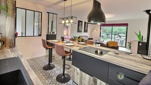 Una cocina moderna con una isla central, taburetes de bar, iluminación colgante y vistas al exterior.