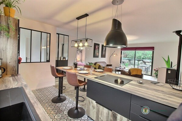 Una cocina moderna con una isla central, taburetes de bar, iluminación colgante y vistas al exterior.