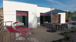 Un patio moderno al aire libre con sillones rojos, una terraza de madera y un muro de piedra.
