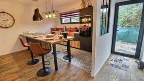 Una cocina moderna con comedor, que cuenta con una mesa de madera, sillas color naranja y un ventanal con vistas al verdor.