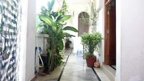 Een smalle gang met planten in potten, een houten deur en een betegelde vloer.