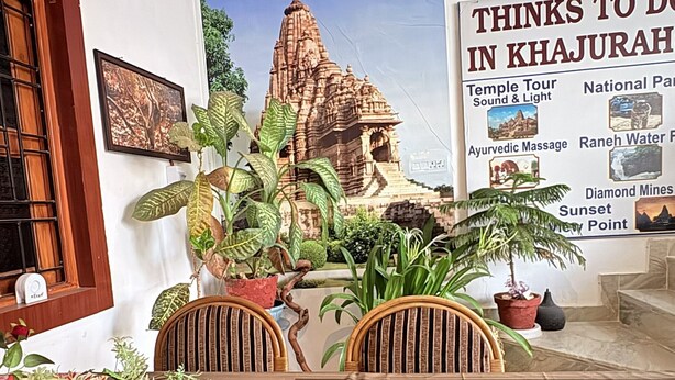 Een lobby met een groot muurdecoratie van een tempel, potplanten, houten meubels en een bord waarop faciliteiten zoals tempeltours en massages staan vermeld.