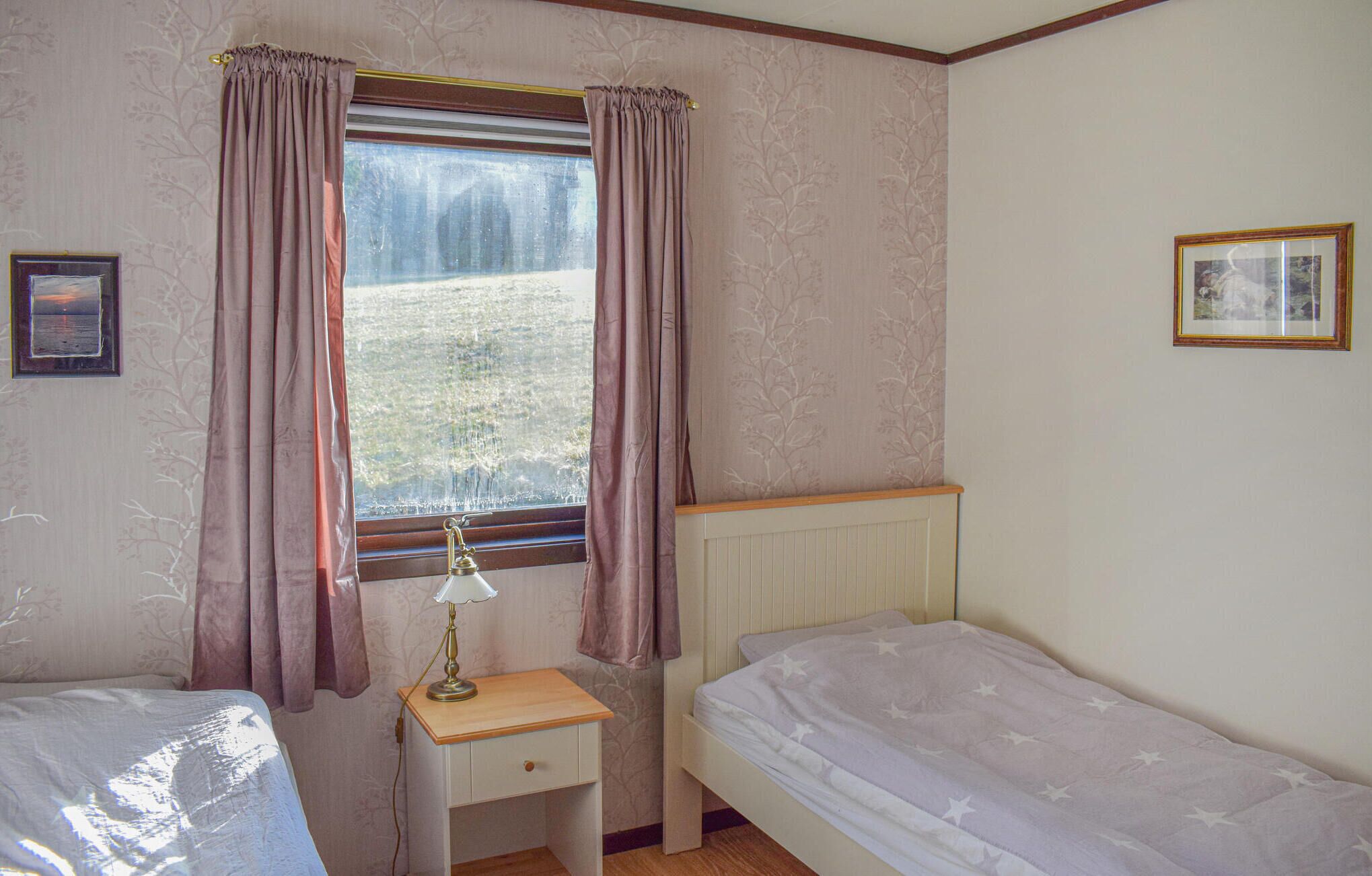 Une chambre avec deux lits simples, une table de chevet avec une lampe, une fenêtre avec des rideaux et un radiateur.