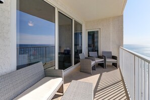 Ein Balkon mit einer Couch und zwei Stühlen, Blick aufs Meer, und einem weißen Geländer.