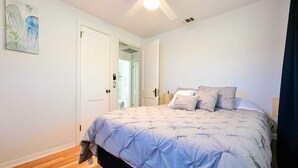 Ein Schlafzimmer mit einem Bett, einem Deckenventilator, einer Tür und einem Bild an der Wand.
