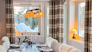 A dining area with a table set for four, a chandelier, and a view of snow-covered trees through a window. - Beautiful home in Noresund with WiFi (Noresund)
