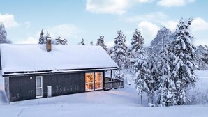A snow-covered cabin with a porch and a chimney, surrounded by snow-laden trees. - Beautiful home in Noresund with WiFi (Noresund)