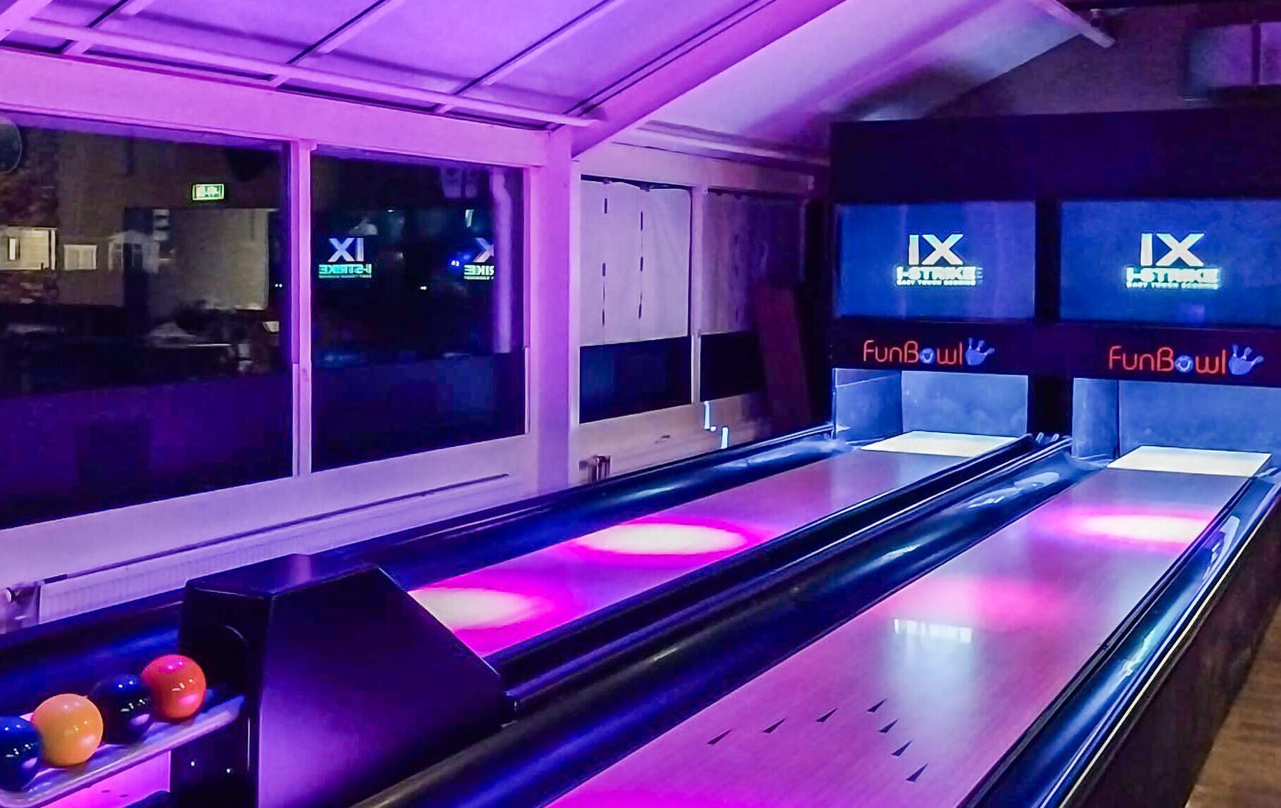 En bowlinghal med flere baner, neonskilte og en række farverige bowlingkugler.