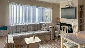 Ein Wohnzimmer mit einer Couch, einem Couchtisch, einem an der Wand montierten Fernseher und einem Essbereich mit Stühlen und einem Tisch.