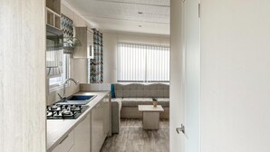 Eine kompakte Küche mit Gasherd, Spüle und moderner Schränke. Eine integrierte Sitzbank mit Kissen befindet sich in der Nähe eines Fensters mit Jalousien.