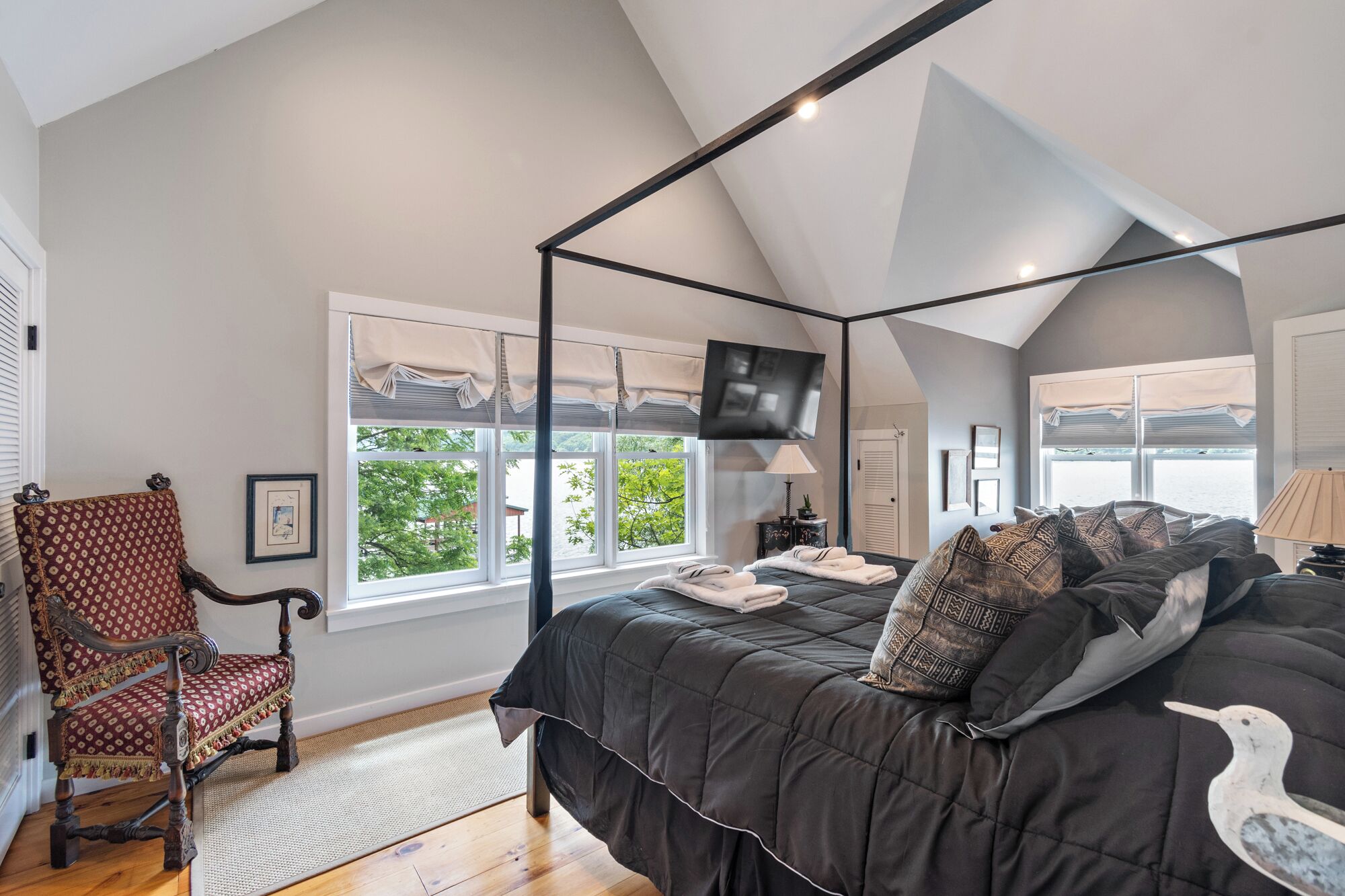 A bedroom with a four-poster bed, a chair, a television, and a view of the outdoors.