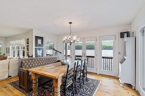 A spacious dining area with a wooden table and chairs, a chandelier, and a view of a lake through large sliding doors.