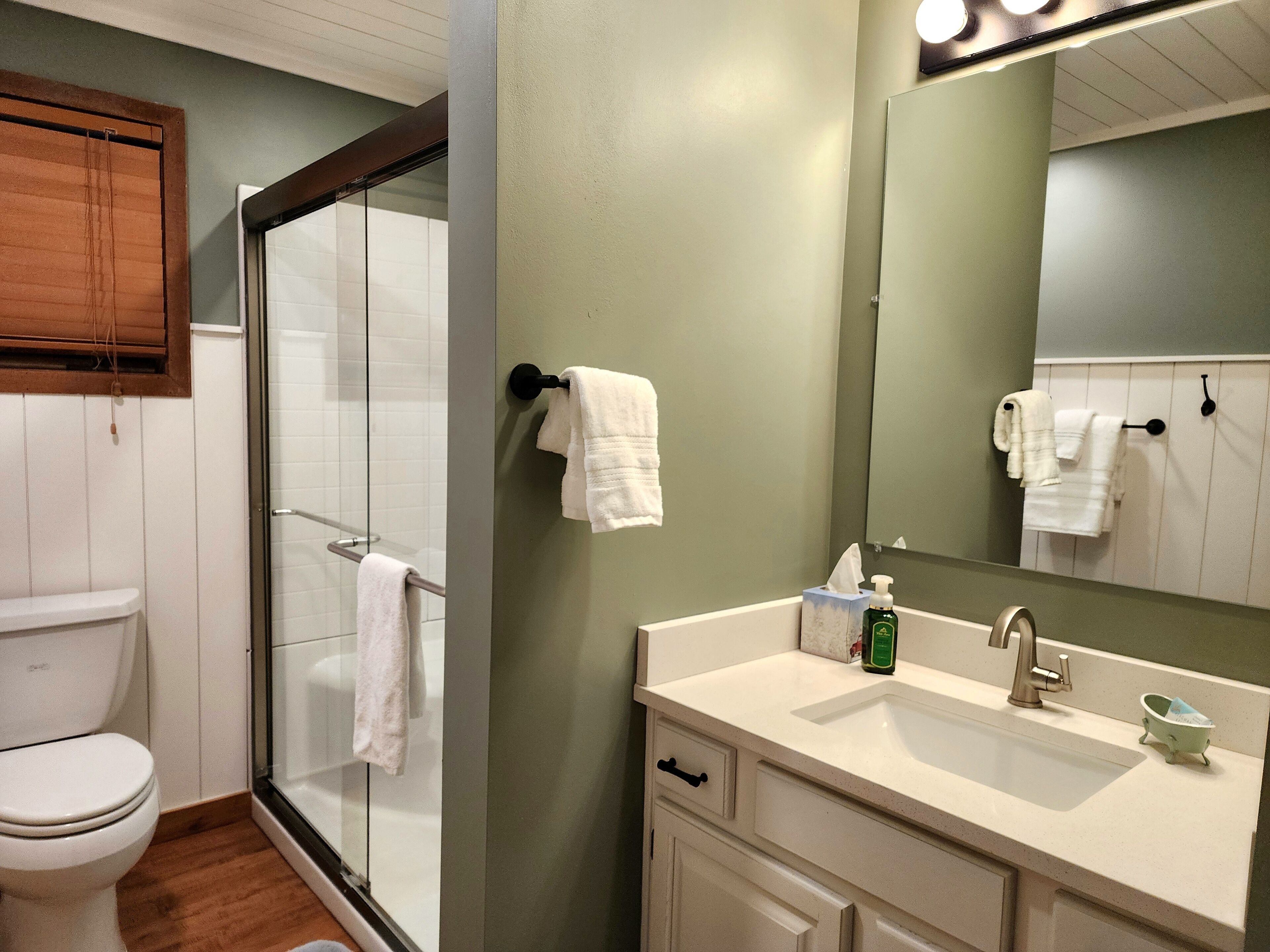 Une salle de bain avec une douche à parois de verre, des toilettes blanches, un lavabo avec un miroir et un porte-serviettes avec plusieurs serviettes.