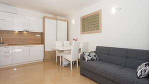 A modern kitchen with white cabinets, a dining table with chairs, and a grey sofa with patterned cushions. - Awesome apartment in Podgrade with WiFi (Podgrade)