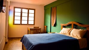 A bedroom with a bed, a chair, a table, and a window.