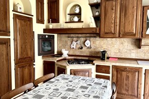 A kitchen with wooden cabinets, a stove, and a dining table with a patterned tablecloth. - S287 - Sirolo, villa with garden near the centre (Sirolo)