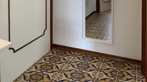 Un passadís amb un paviment de rajoles estampades, una porta blanca amb marc de fusta i un mirall a la paret.