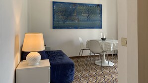 Habitació amb un quadre abstracte blau, una taula blanca i un suport de vidre per a espelma, i un terra amb un disseny decoratiu.