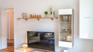 Ein Wohnzimmer mit Flachbildfernseher, einer Ablage mit Dekoration und einem Schrank mit Gläsern.