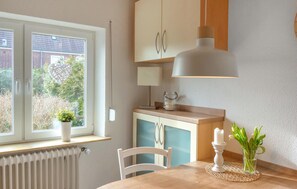 Una cocina con ventana, un radiador, una mesa con una vela y un florero con flores.