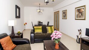 A living room with a sofa, a coffee table with a vase of flowers, a TV stand, and a painting on the wall. - Casa Gloria, easy walk to city centre (Lagos)