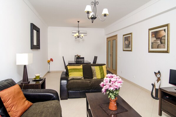 A living room with a sofa, a coffee table with a vase of flowers, a TV stand, and a painting on the wall. - Casa Gloria, easy walk to city centre (Lagos)