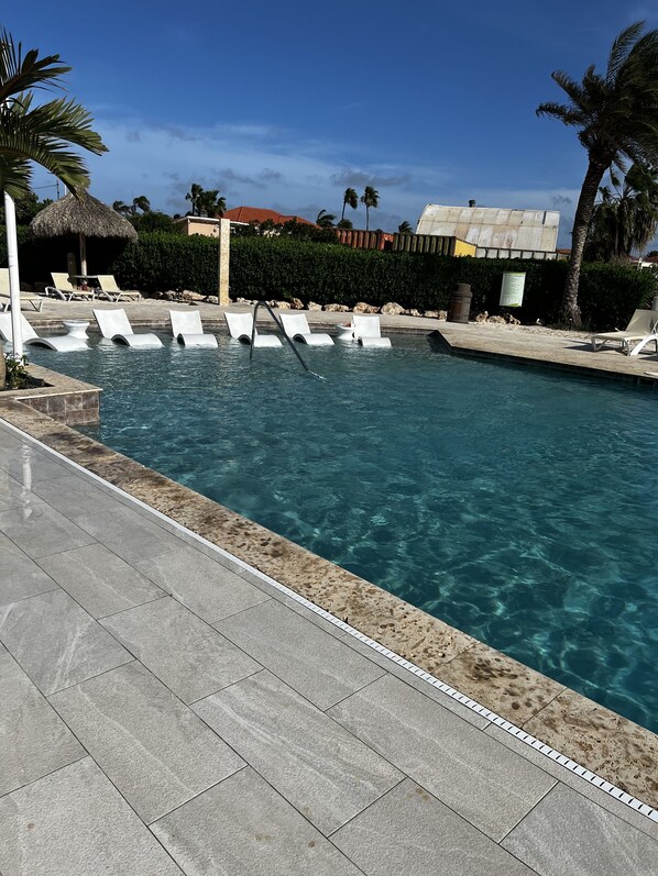 Una piscina cristalina con sillas reclinables blancas y un solárium con baldosas.