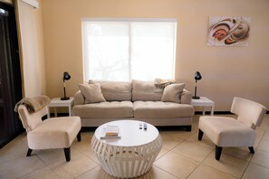 Una sala de estar con un sofá color beige, dos sillones, una mesa de centro redonda y dos mesas auxiliares con lámparas.