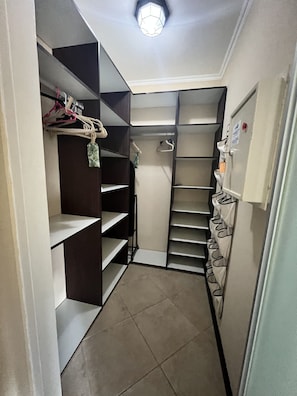 A narrow walk-through closet with multiple shelves and hanging space, a door with a lock, and a light fixture on the ceiling.