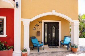 Una entrada de edificio con una puerta negra, dos sillas azules y una pared con la inscripción 'Faith Hope Love 93'.