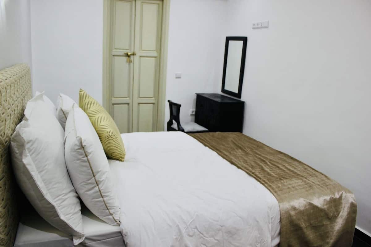 A bedroom with a bed, pillows, a bedside table, a mirror, and a wardrobe.