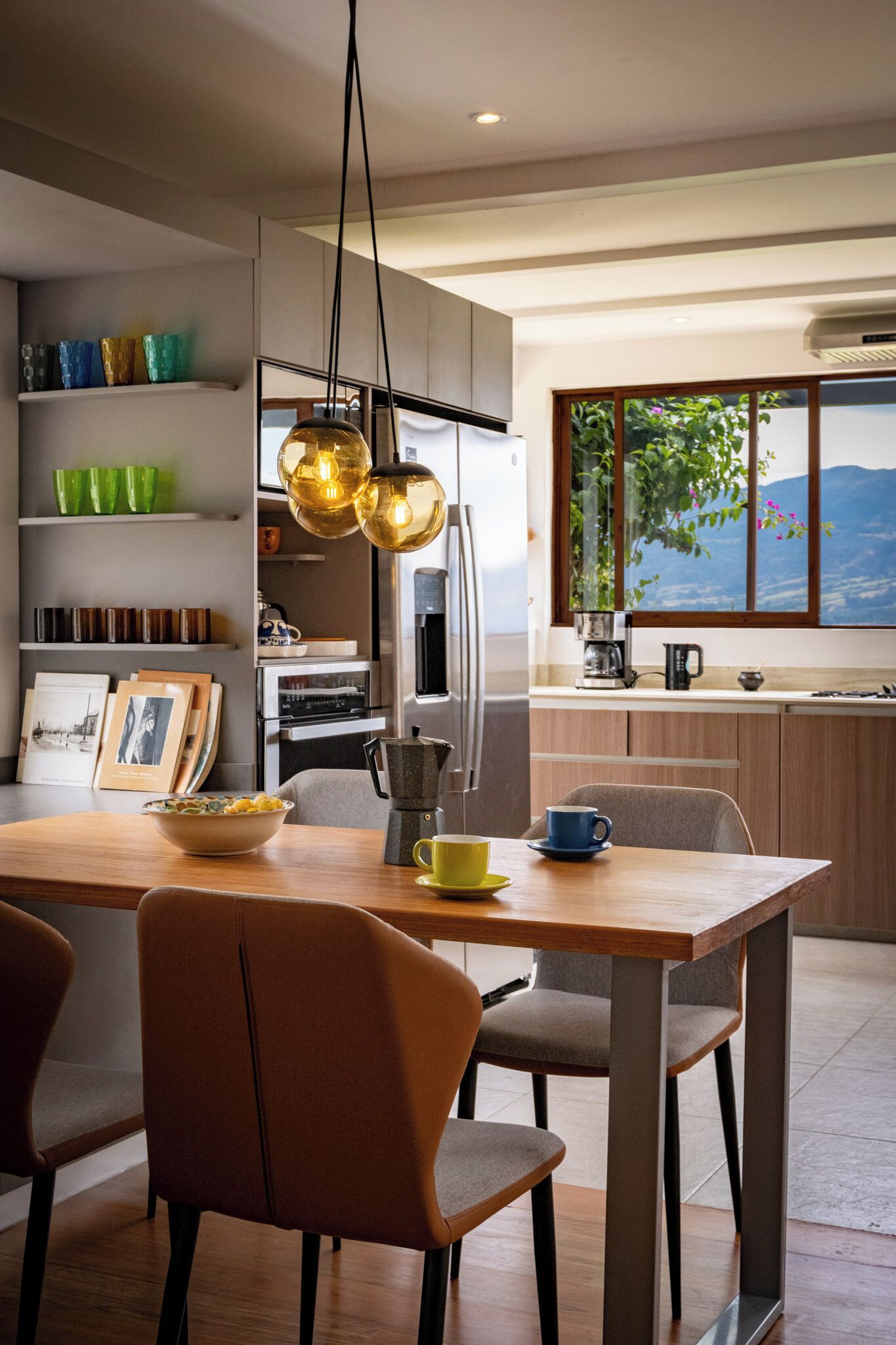 A modern kitchen with a dining table, chairs, and a view of the outdoors through a window.