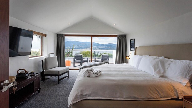 Ein Hotelzimmer mit einem großen Bett, einem Fernseher, einem Schreibtisch und Blick ins Freie.