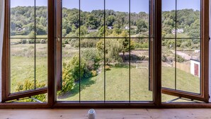 Une pièce dotée d’une grande porte-fenêtre coulissante donnant sur un paysage verdoyant, avec des arbres et quelques maisons.