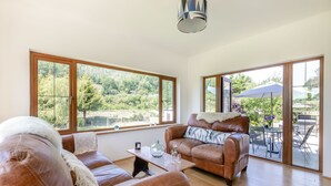 Un salon spacieux, doté de canapés en cuir, d’une table basse et de grandes fenêtres donnant sur un jardin luxuriant.